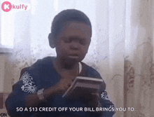 a young boy is sitting in a chair holding a credit card and a calculator .