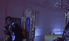 a man and a woman are sitting on thrones in a room . the woman is wearing a crown .