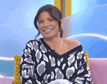 a woman in a black and white sweater smiles while sitting on a pink couch