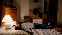 a man is laying on a bed in a room with boxes and a lamp