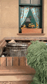 a trash can in front of a window with flowers in a planter