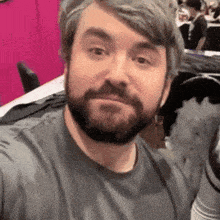 a man with a beard is taking a selfie with a pink background