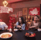 three people are sitting at a table with bowls of food in front of a sign that says ' piciest cup korea '