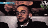 a man wearing glasses and earbuds is watching a soccer game