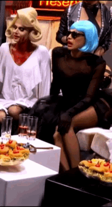 a woman in a blue wig sits at a table with a pepsi sign in the background
