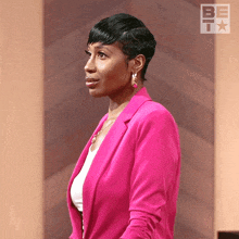 a woman in a pink jacket and earrings stands in front of a wall with the letter b on it