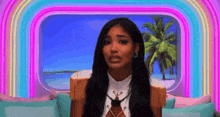 a woman with long hair is sitting on a couch in front of a window with a palm tree in the background .