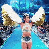 a woman wearing wings and a belt stands on a stage in front of a crowd