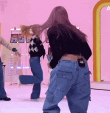 a woman in a black sweater and blue jeans stands in front of a pink wall