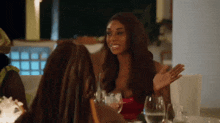 a group of women are sitting at a table with wine glasses and talking to each other .