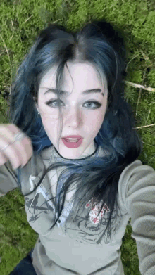 a girl with blue hair is taking a selfie while laying on the grass .