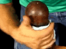 a man in a green shirt is holding a large brown egg in his hand .