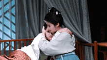 a woman is hugging another woman who is laying in bed
