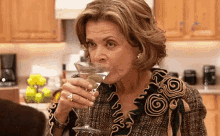 a woman is drinking a martini in a kitchen while wearing a ruffled top .