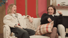 two women are sitting on a couch laughing and one is wearing a watch