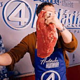a man wearing a blue apron that says " antorcha humana " holds a large piece of meat