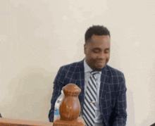 a man in a suit and tie is sitting at a table with a bottle of water in front of him .