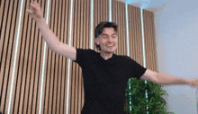 a man in a black shirt is standing with his arms outstretched in front of a wooden wall .