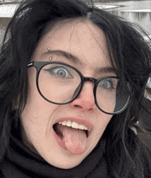 a woman wearing glasses sticks her tongue out and has a piercing in her eyebrow