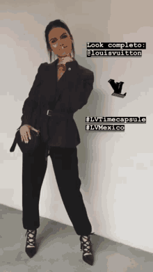 a woman in a black suit is standing in front of a white wall with louis vuitton written on it