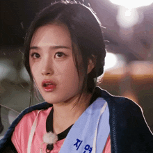 a woman wearing a pink shirt and a blue sash that says " 지영 " on it