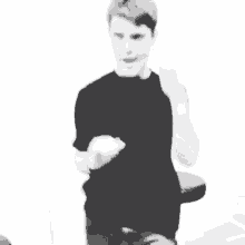 a black and white photo of a young man in a black shirt standing next to a drum stool .