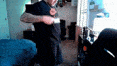 a man in a black shirt is holding a knife in a bedroom .