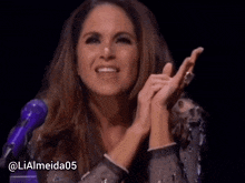 a woman applauds in front of a purple microphone with the hashtag @ lialmeida05