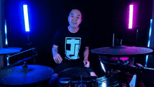 a man wearing a black shirt with the letter t on it playing drums