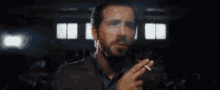 a man with a beard is smoking a cigarette in front of a crowd in a dark room .
