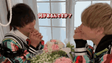 two young men are holding hands in front of a bouquet of pink and white flowers in a room
