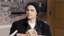 a man wearing a black beanie is holding a notebook and pen