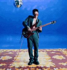 a man in a green suit is playing a bass guitar in front of a disco ball