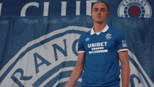 a man wearing a blue shirt that says unibet stands in front of a rangers banner