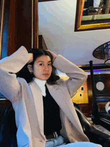 a woman with her hands on her head is wearing a tan coat