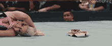 a woman is laying on the floor in a wrestling ring with a magazine on the ground .