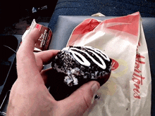 a person holding a chocolate donut next to a bag that says tim hortons on it