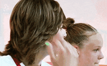 a girl with green nail polish is touching a boy 's ear