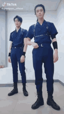 two men are standing next to each other wearing blue jumpsuits and black boots .