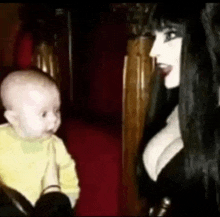 a woman in a black dress is holding a baby and talking to it .