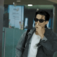 a man wearing sunglasses and a denim jacket is smoking a cigarette .