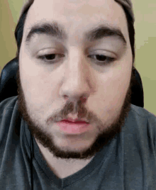 a man with a beard is wearing a hat and a grey shirt