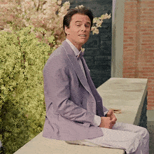 a man in a purple suit and bow tie sits on a ledge