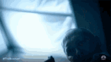 a person is laying on a bed in front of a window with a light coming out of it .