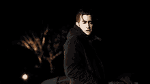 a man in a black coat is standing in the dark in front of a car .
