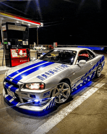 a silver and blue sports car is parked at a gas pump