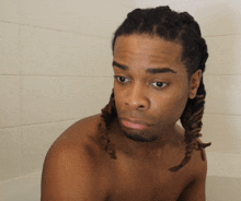 a shirtless man with dreadlocks looks at the camera with a serious look on his face