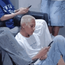 a man with blonde hair is sitting on a couch using a cell phone .