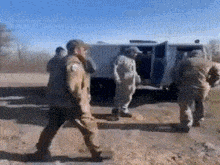 a group of soldiers are walking down a dirt road in front of a van .