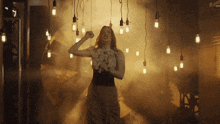 a woman in a white dress is dancing in a room with smoke and lights hanging from the ceiling